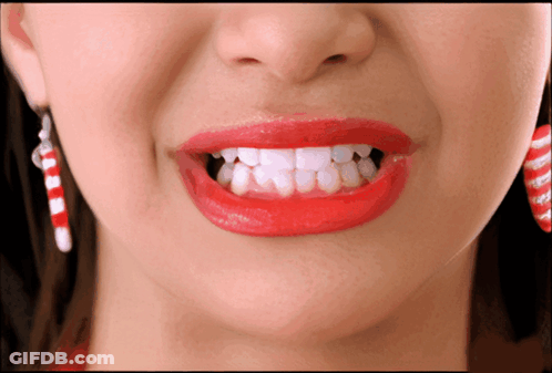 A Woman Wearing Red Lipstick And Candy Cane Earrings GIF