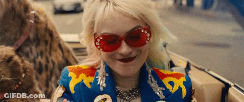 A Woman Wearing Red Sunglasses And A Colorful Jacket Smiles While Sitting In A Car GIF