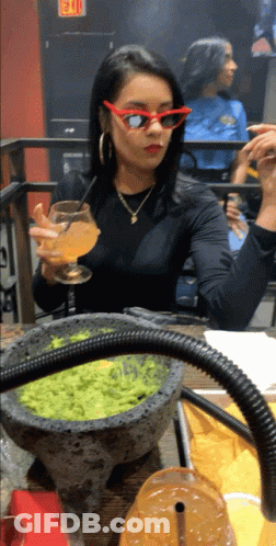 A Woman Wearing Red Sunglasses Sits At A Table With A Bowl Of Guacamole On It GIF