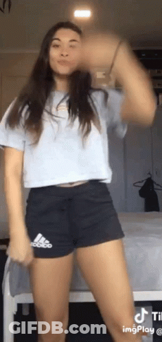 A Woman Wearing Shorts And A Crop Top Is Dancing In A Bedroom . GIF