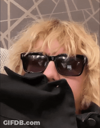 A Woman Wearing Sunglasses And A Black Jacket Covering Her Face GIF