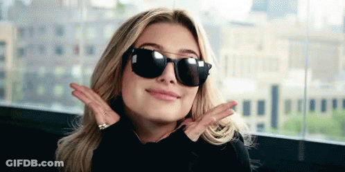 A Woman Wearing Sunglasses And A Black Shirt Is Making A Peace Sign With Her Hands . GIF