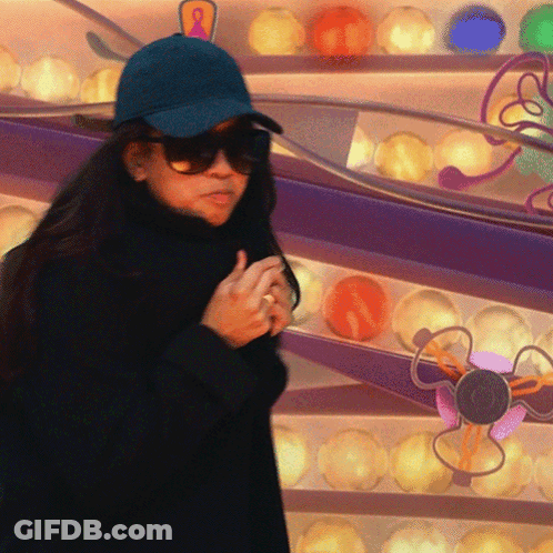 A Woman Wearing Sunglasses And A Blue Hat Stands In Front Of A Display Of Colorful Balls GIF