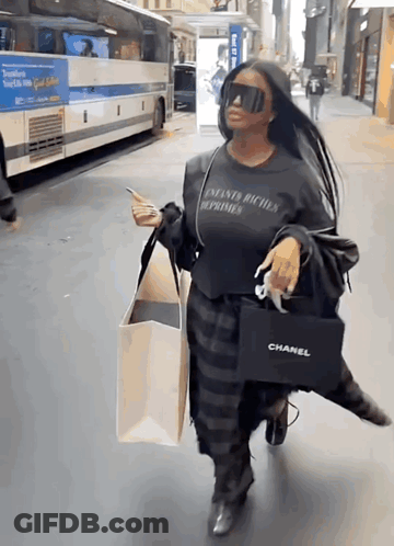 A Woman Wearing Sunglasses And A Chanel Bag Walks Down A Street GIF