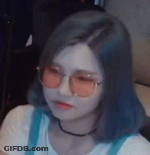 A Woman Wearing Sunglasses And A Choker Is Sitting On A Couch . GIF