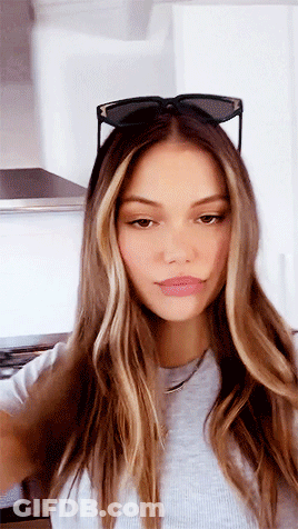 A Woman Wearing Sunglasses And A Gray Shirt Is Taking A Selfie . GIF