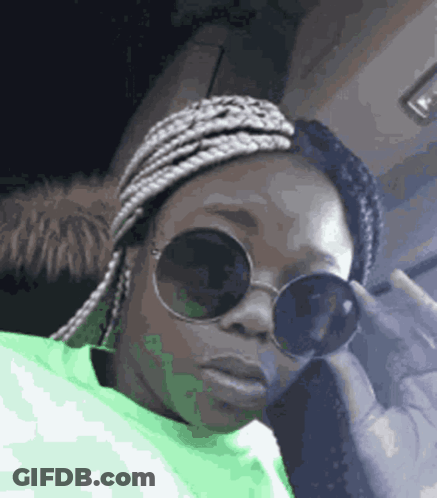 A Woman Wearing Sunglasses And A Green Sweater Is Sitting In A Car . GIF