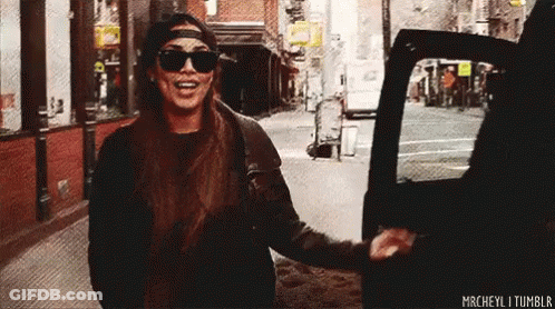 A Woman Wearing Sunglasses And A Hat Is Getting Out Of A Car On A City Street . GIF