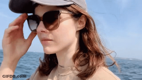 A Woman Wearing Sunglasses And A Hat Looks At The Camera GIF