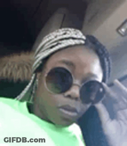 A Woman Wearing Sunglasses And A Head Scarf Is Sitting In A Car . GIF