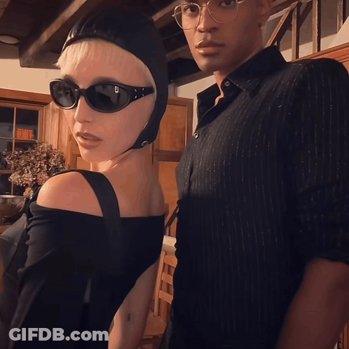 A Woman Wearing Sunglasses And A Helmet Stands Next To A Man GIF