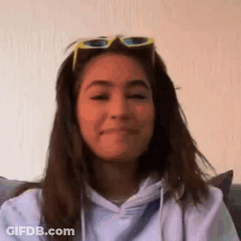 A Woman Wearing Sunglasses And A Hoodie Is Making A Face . GIF