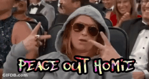 A Woman Wearing Sunglasses And A Hoodie Is Sitting In A Crowd Of People And Making A Peace Sign .. GIF