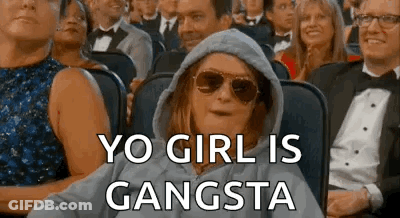 A Woman Wearing Sunglasses And A Hoodie Is Sitting In A Crowd Of People And Says `` Yo Girl Is Gangsta '' . GIF