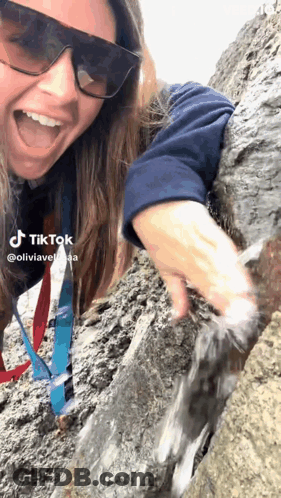 A Woman Wearing Sunglasses And A Lanyard Is Playing With Water On A Rock Wall . GIF