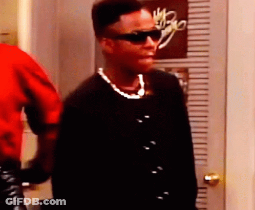 A Woman Wearing Sunglasses And A Pearl Necklace Is Standing Next To A Door . GIF