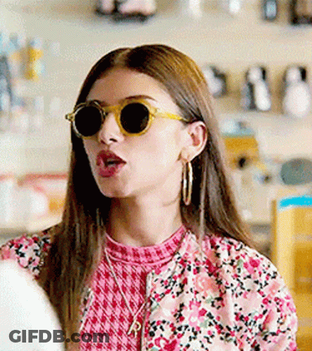 A Woman Wearing Sunglasses And A Pink Floral Jacket Is Making A Funny Face . GIF
