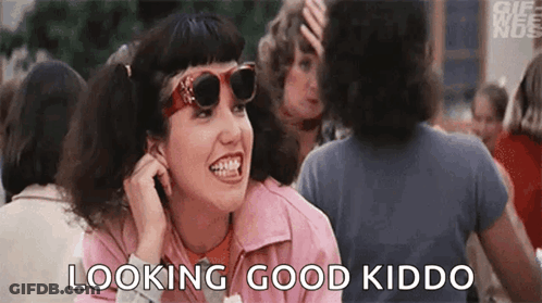 A Woman Wearing Sunglasses And A Pink Jacket Is Sitting In A Crowd Of People And Talking On A Cell Phone . GIF