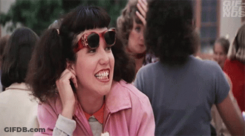 A Woman Wearing Sunglasses And A Pink Jacket Is Smiling In A Crowd . GIF