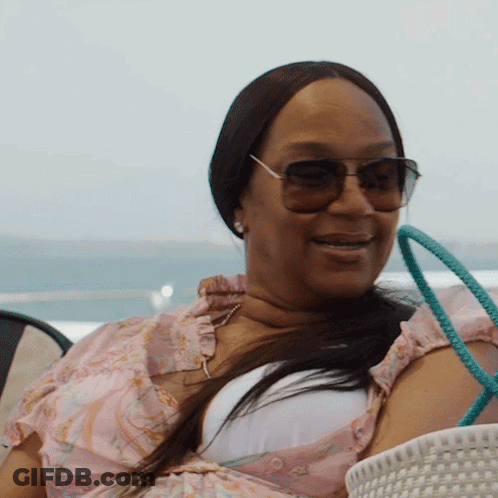 A Woman Wearing Sunglasses And A Pink Top Smiles GIF