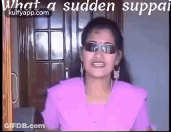 A Woman Wearing Sunglasses And A Purple Shirt Is Standing In Front Of A Door And Talking . GIF