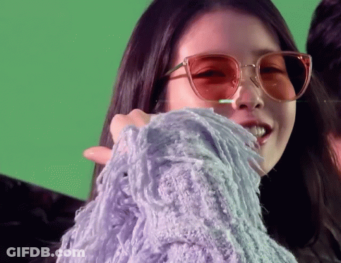 A Woman Wearing Sunglasses And A Purple Sweater On A Green Background GIF