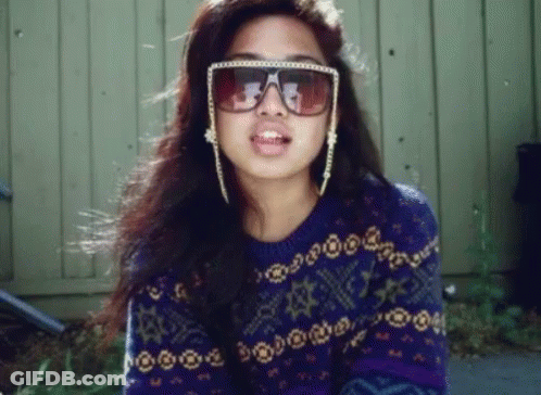 A Woman Wearing Sunglasses And A Purple Sweater With Stars On It GIF