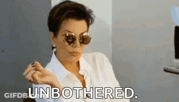 A Woman Wearing Sunglasses And A White Shirt Is Sitting In A Chair And Smoking A Cigarette . GIF