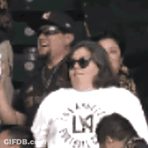 A Woman Wearing Sunglasses And A White Shirt With The Letter L On The Back GIF