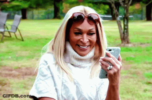 A Woman Wearing Sunglasses And A White Sweater Is Looking At Her Phone GIF
