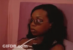 A Woman Wearing Sunglasses And A White Tank Top Is Sitting On A Bed GIF