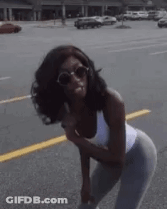 A Woman Wearing Sunglasses And A White Tank Top Is Standing On The Side Of The Road . GIF