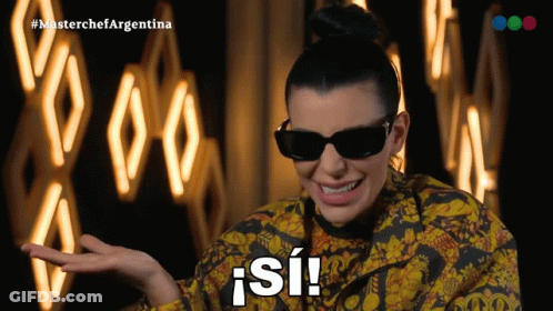 A Woman Wearing Sunglasses And A Yellow And Black Jacket Says " Si " GIF