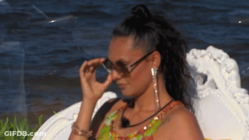 A Woman Wearing Sunglasses And Earrings Is Sitting On A Chair Near The Water . GIF