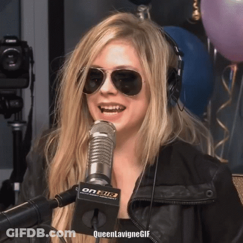 A Woman Wearing Sunglasses And Headphones Is Smiling In Front Of A Microphone That Says On Air On It GIF