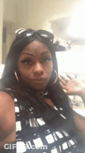 A Woman Wearing Sunglasses And Hoop Earrings Is Making A Funny Face GIF