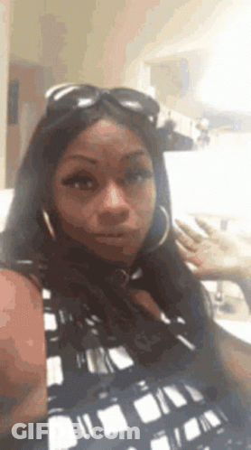 A Woman Wearing Sunglasses And Hoop Earrings Is Taking A Selfie GIF