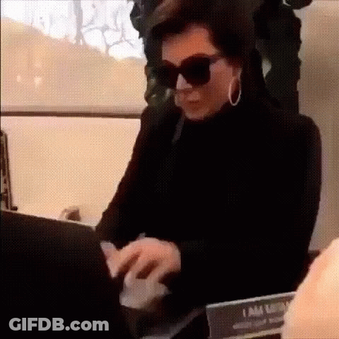 A Woman Wearing Sunglasses And Hoop Earrings Is Typing On A Laptop Computer . GIF