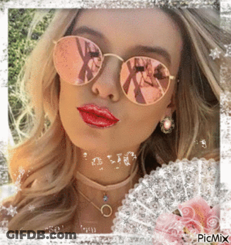 A Woman Wearing Sunglasses And Red Lipstick Is Surrounded By Flowers GIF