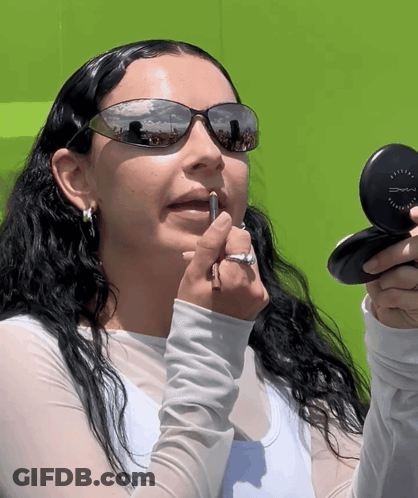 A Woman Wearing Sunglasses Applying Lipstick With A Mac Compact GIF