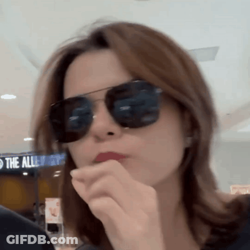 A Woman Wearing Sunglasses In Front Of A Sign That Says The Alleyways GIF