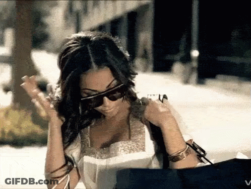A Woman Wearing Sunglasses Is Holding A Bag And Looking At Something GIF