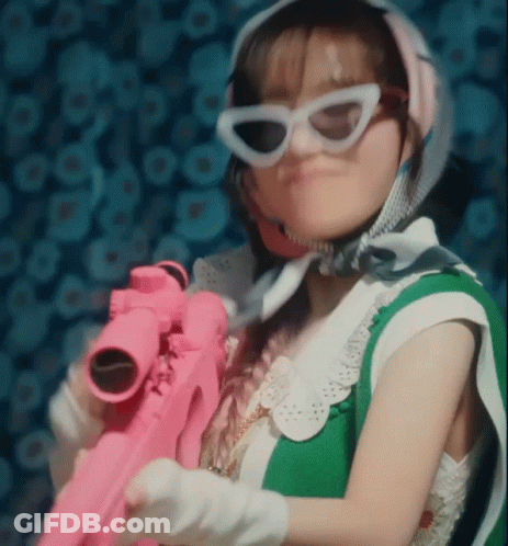 A Woman Wearing Sunglasses Is Holding A Pink Toy Gun . GIF