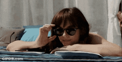 A Woman Wearing Sunglasses Is Laying On A Towel On A Beach . GIF