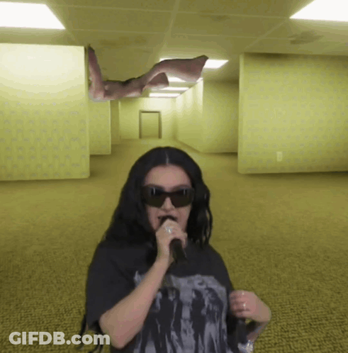 A Woman Wearing Sunglasses Is Singing Into A Microphone In A Hallway GIF