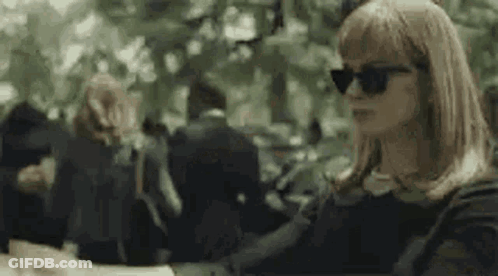 A Woman Wearing Sunglasses Is Sitting At A Table In A Crowded Park . GIF