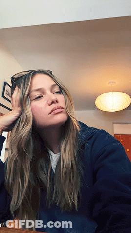 A Woman Wearing Sunglasses Is Sitting At A Table With Her Hand On Her Face GIF