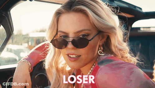 A Woman Wearing Sunglasses Is Sitting In A Car With The Word Loser Written On The Side GIF