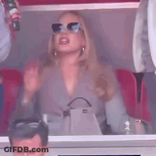 A Woman Wearing Sunglasses Is Sitting In A Stadium Holding A Bottle Of Coca Cola . GIF