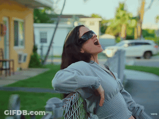 A Woman Wearing Sunglasses Is Sitting On A Chain Link Fence With Her Mouth Open GIF